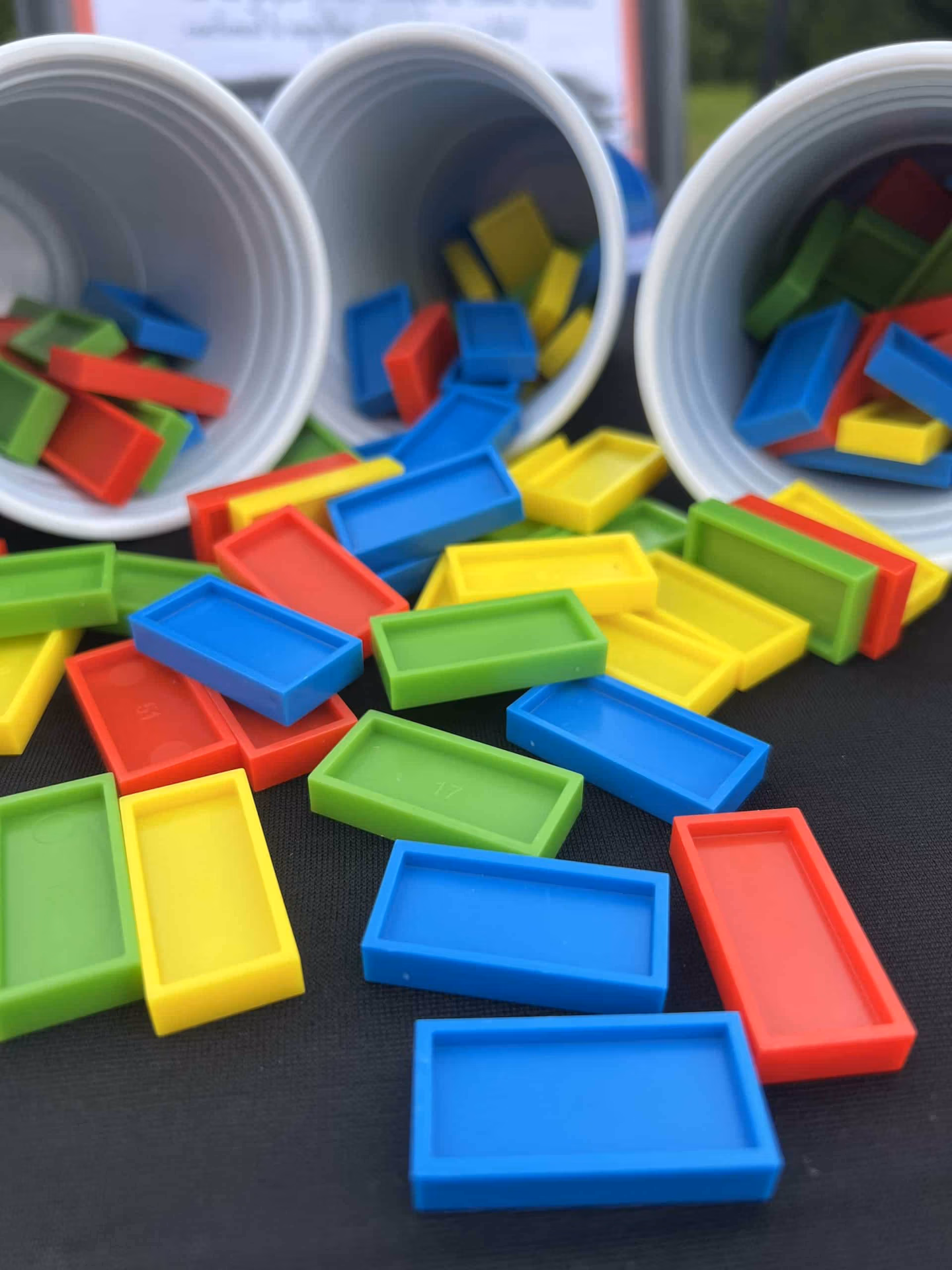 Lots de dominos étalés et 3 gobelets en arriÚre plan contenant des dominos