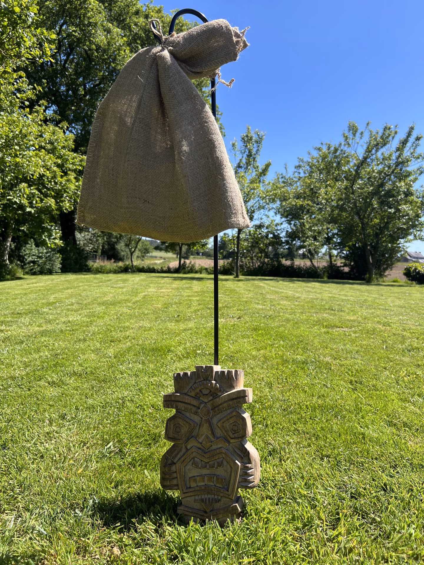 Vue d'ensemble du sac de jute du Tangram accroché par un pied de berger et un totem positionné au pied