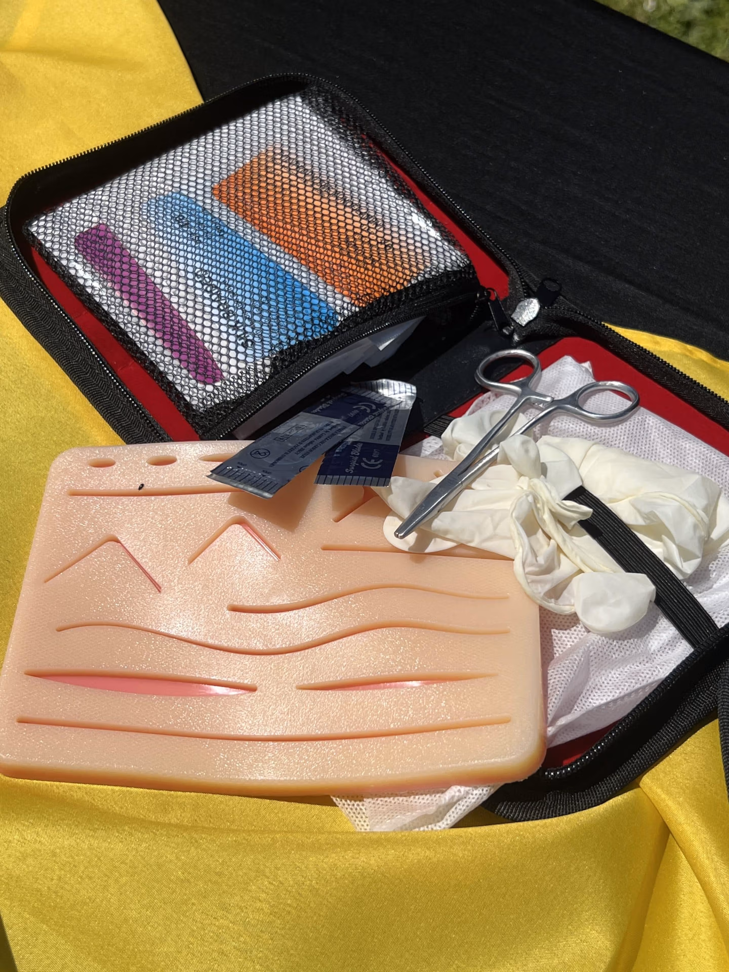 Vue sur le contenant d'une valisette de suture d'exercice avec aiguille, ciseau et peau factice